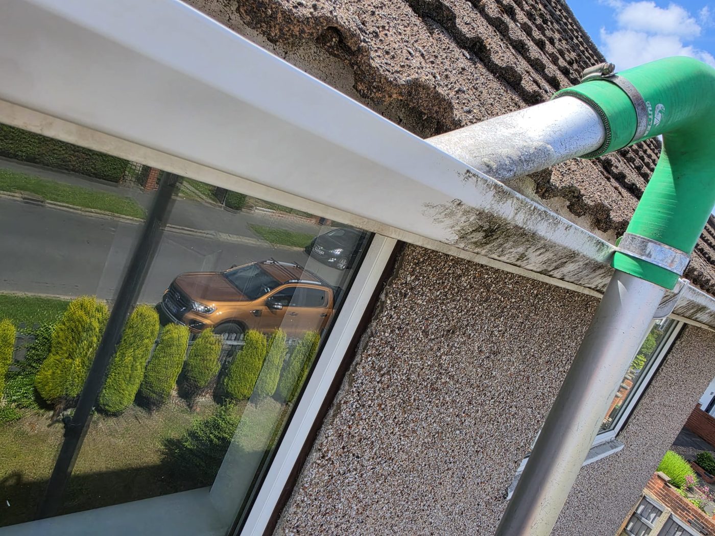 Gutter vacuum cleaning a gutter alongside white fascia with house reflected in the window