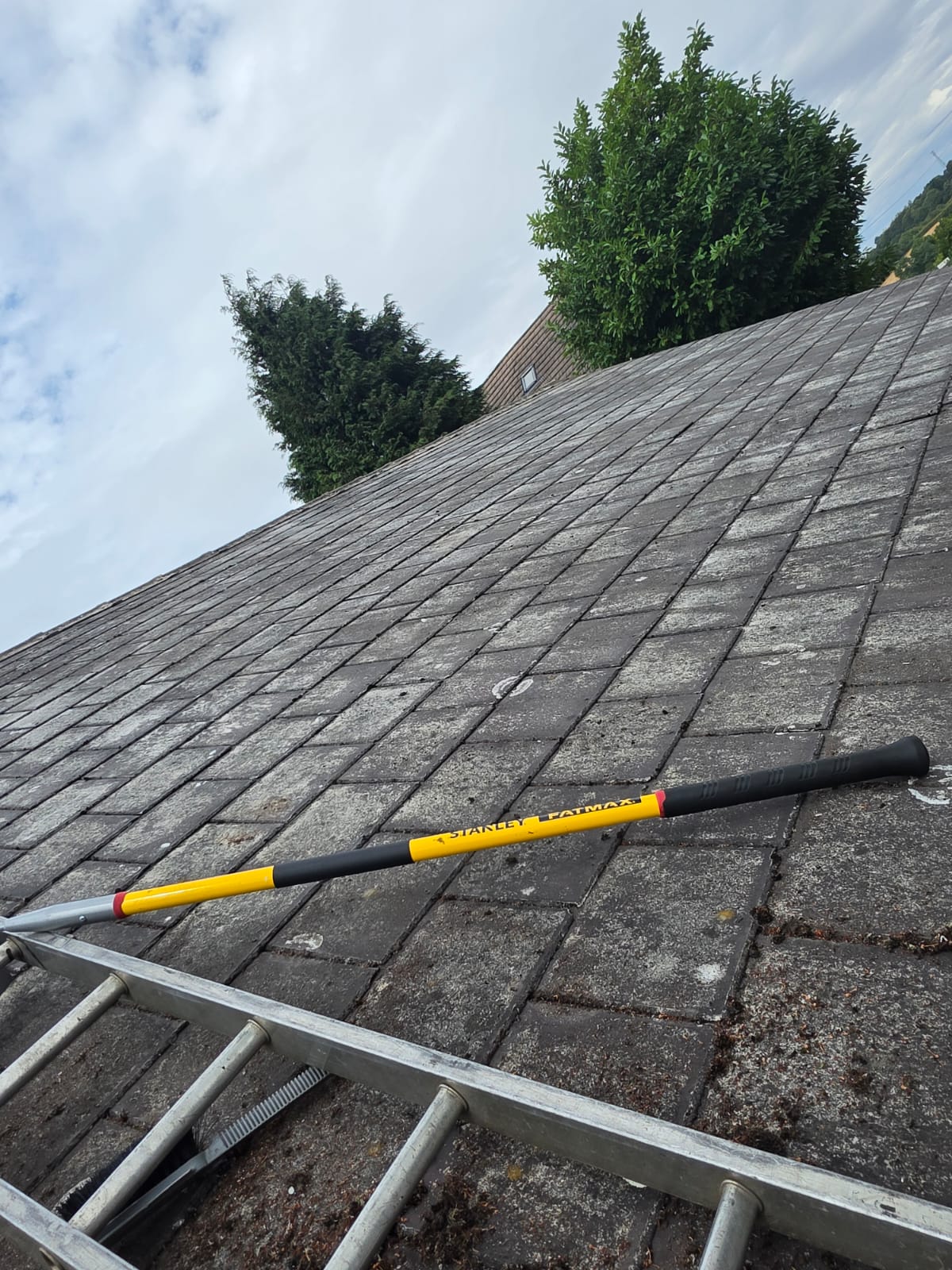 Telescopic pole laid across roof tiles part way through a moss scrape and biocide treatment